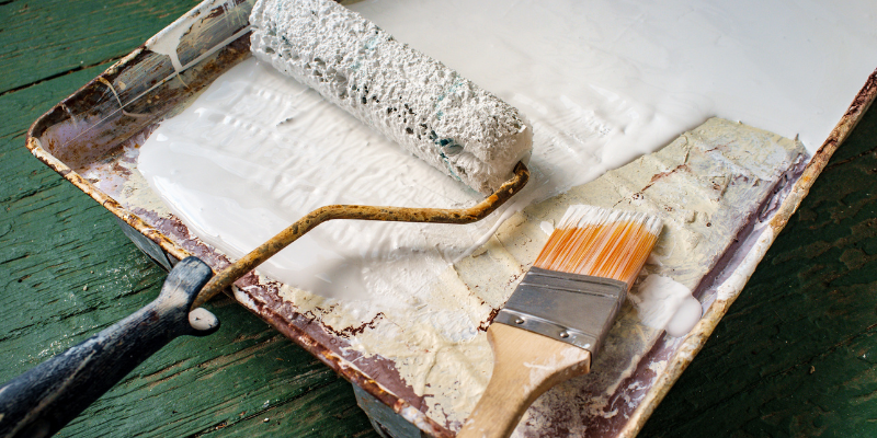 Roller and paint brush dipped in white paint in a tray