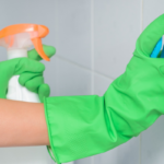 Person wearing green gloves and scrubbing a wall