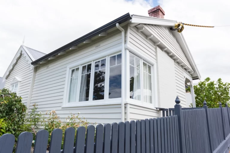 Front of weatherboard house painted off white with blue fence
